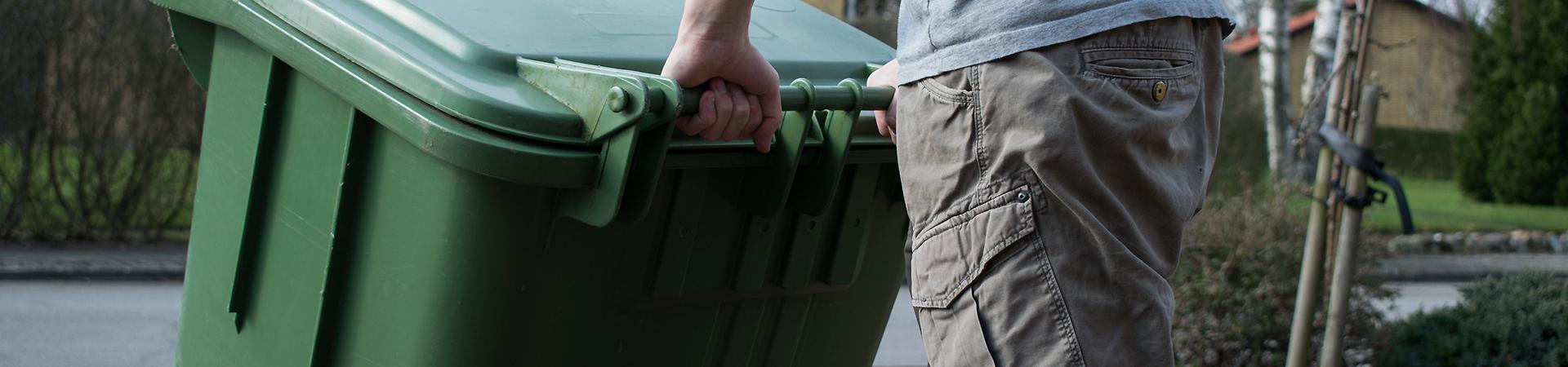 En mand som trækker en grøn affaldsbeholder i plast